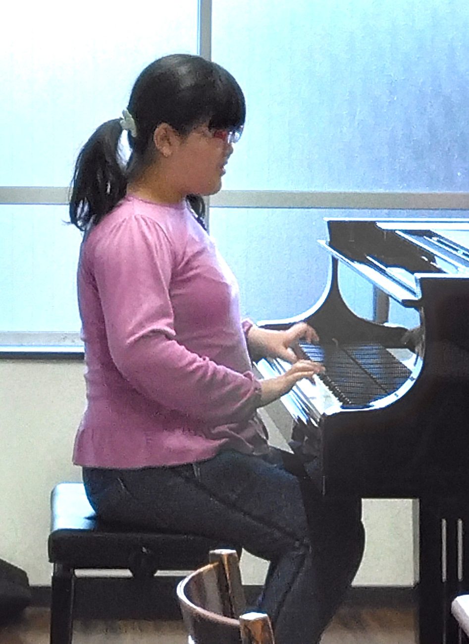 窓辺のグランドピアノに向かって演奏するお子さん