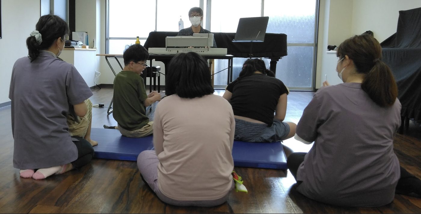 療育室で職員と子どもたちが演奏を囲んで座っている様子